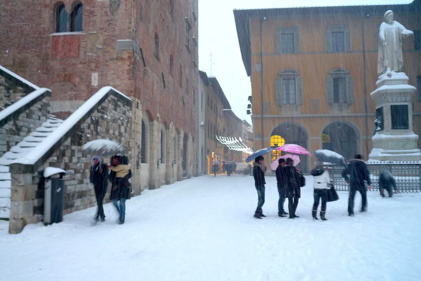Piazza del Comune a Prato imbiancata dalla neve, con i passanti sotto gli ombrelli